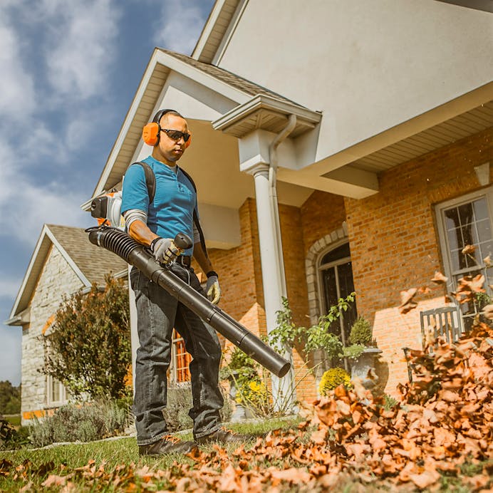 Man in STIHL protective gear blowing leaves in front of house with the BR 200
