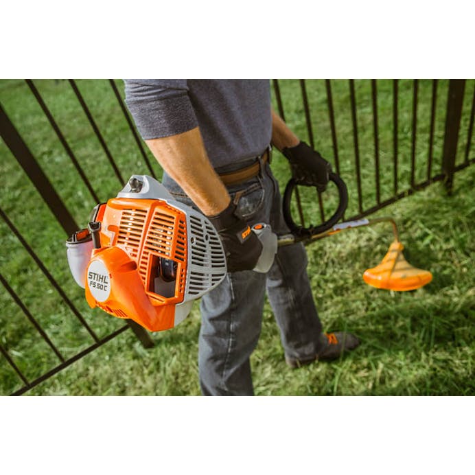 Close up of man standing by fence holding STIHL FS 50 C-E trimmer