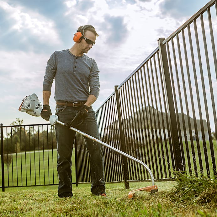 Man using STIHL FS 50 C-E to trim along fence line