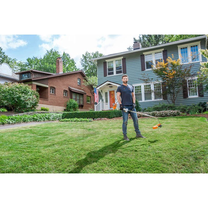 Man standing on lawn in front of house holding the FS 38 trimmer
