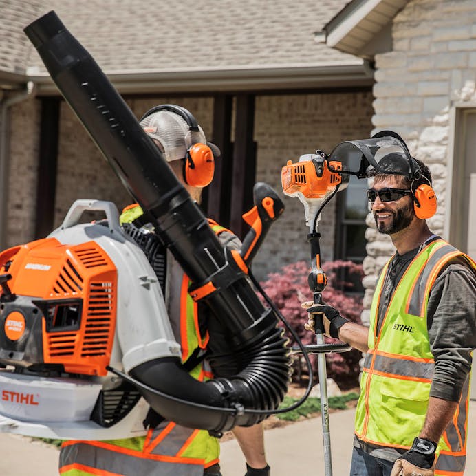 Man holding FS 94 R standing beside another man carrying a STIHL backpack blower