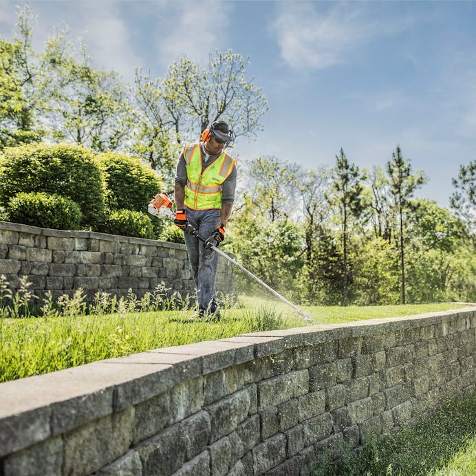 Man trimming along the edge of a stone wall with FS 94 R