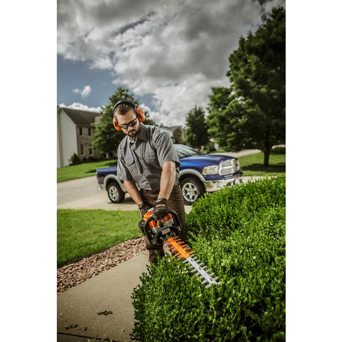 Man standing of sidewalk using the HS 82 R to trim hedges
