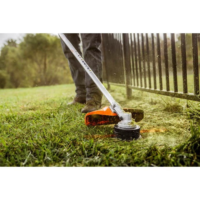 Close up of man using FS 131 R to trim fence line