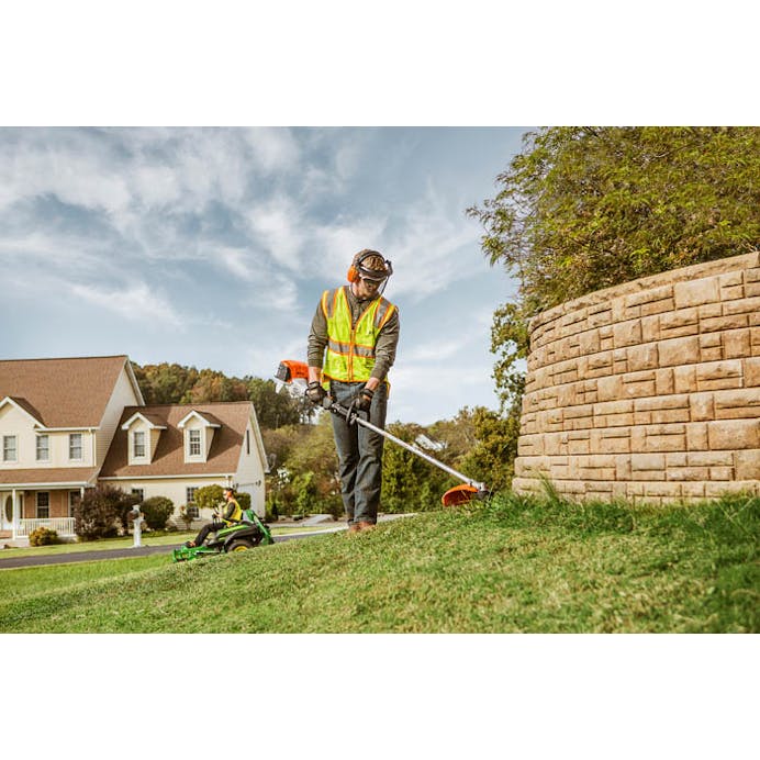 Man in STIHL protective gear trimming along stone wall using the FS 111 RX