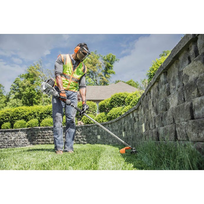 Man in STIHL protective gear trimming along the edge of a stone wall with the FS 91 R