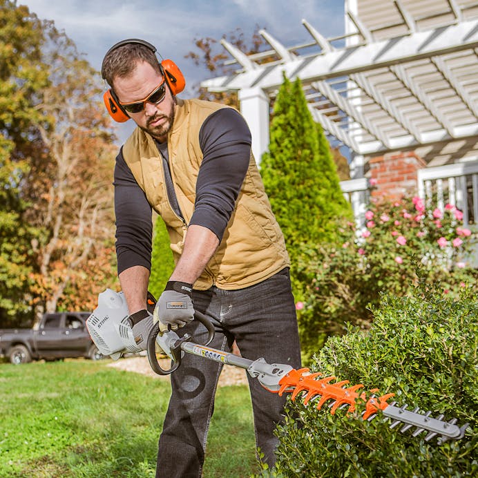 Close up of man trimming bush in front of a pergola using the HL 56 K (0°)
