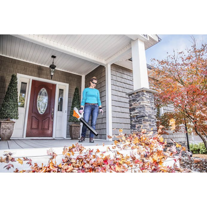Woman blowing leaves on front porch outside house with the BGA 45