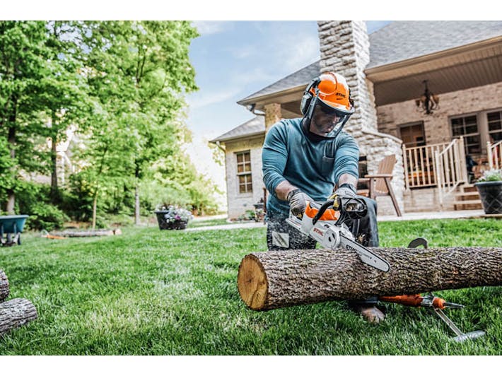 Man cutting log with MSA 120 chainsaw in backyard