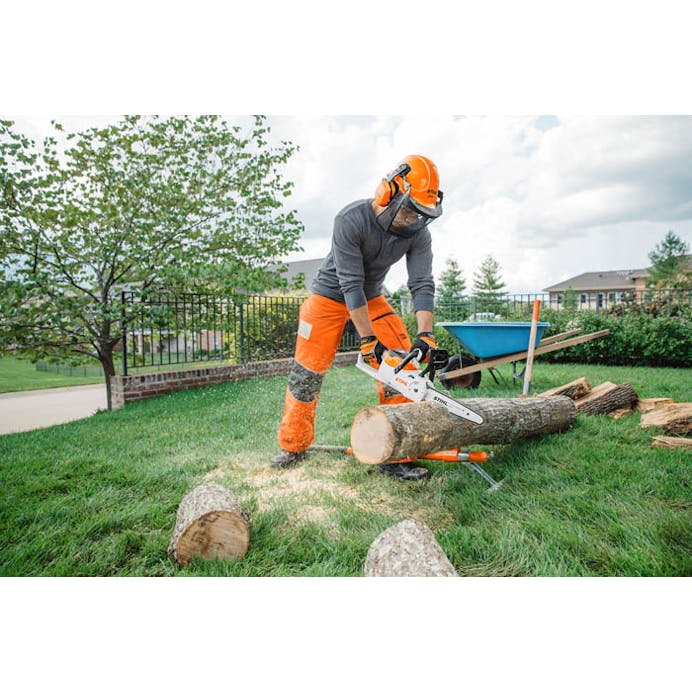 Man cutting log with MSA 120 chainsaw in side yard