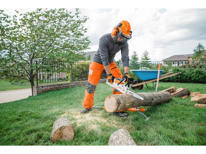 Man cutting log with MSA 120 chainsaw in side yard