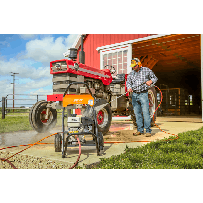 Man standing outside of a barn cleaning off the pavement using the 25' high pressure hose extension 