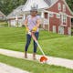 Woman using STIHL FSA 30 to trim sidewalk grass wearing STIHL face guard