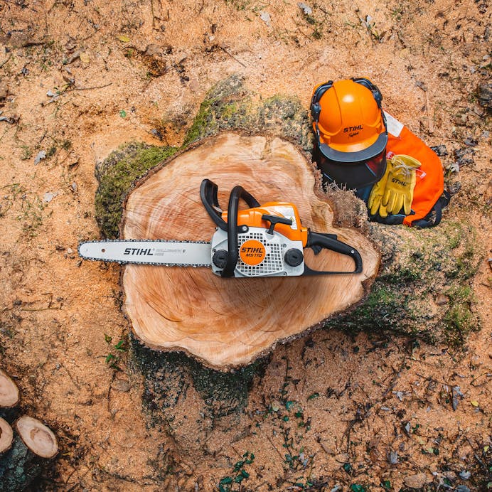 View from above of a STIHL MS 170 Chainsaw resting on a tree stump next to some STIHL protective wear