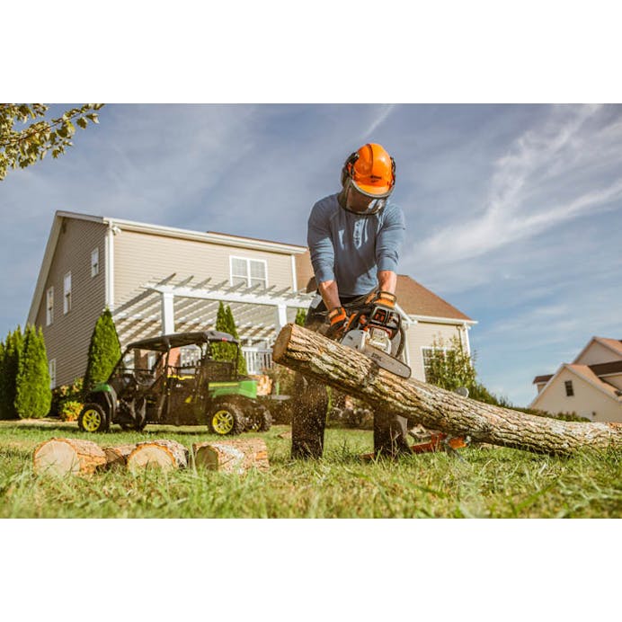Man with protective work gear on cutting log pieces with STIHL MS 180 C-BE Chainsaw in backyard
