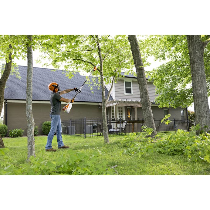 Wide view of a man using the HT-KM Pole Pruner attachment to cut tree branches 