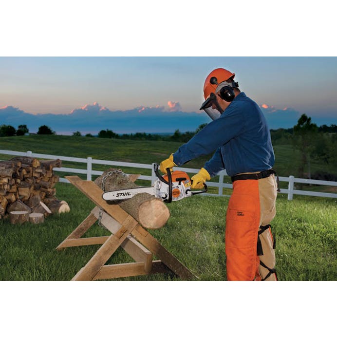 Man cutting a log with the MS 211 Chainsaw as the sun is setting